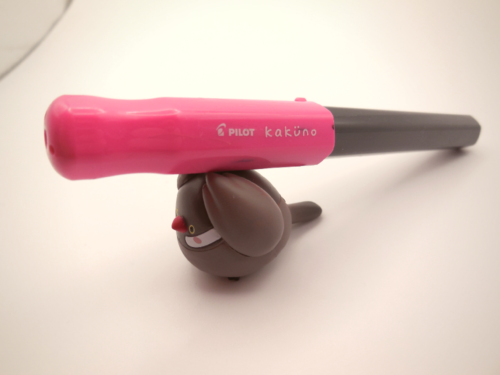 オモチャの文鳥が、パイロット万年筆のカクノを運んでいる写真。カクノの色はピンク。