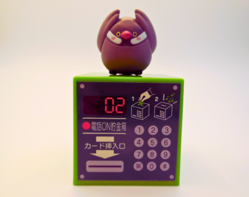 オモチャの文鳥が、公衆電話の形をした貯金箱の上に置かれている写真